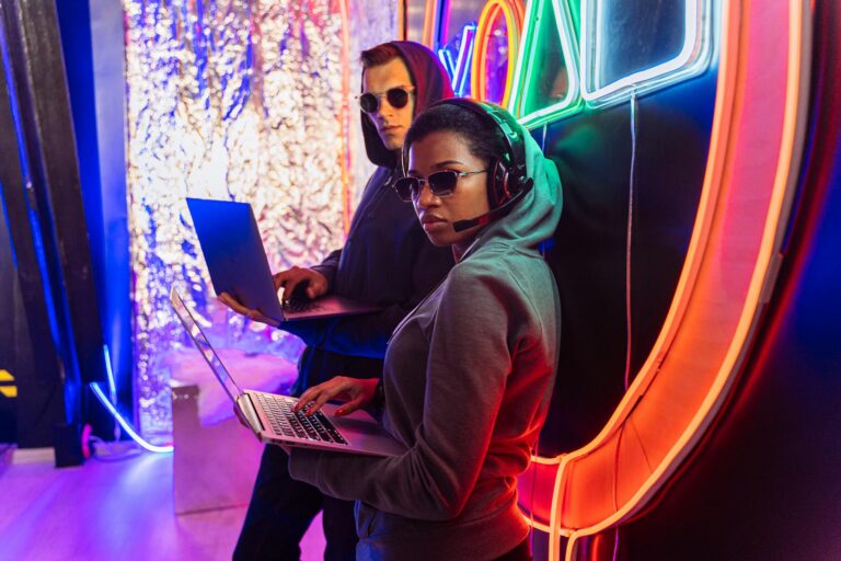 Two tech-savvy individuals with laptops in a vibrant neon setting, embodying futuristic cyber themes.